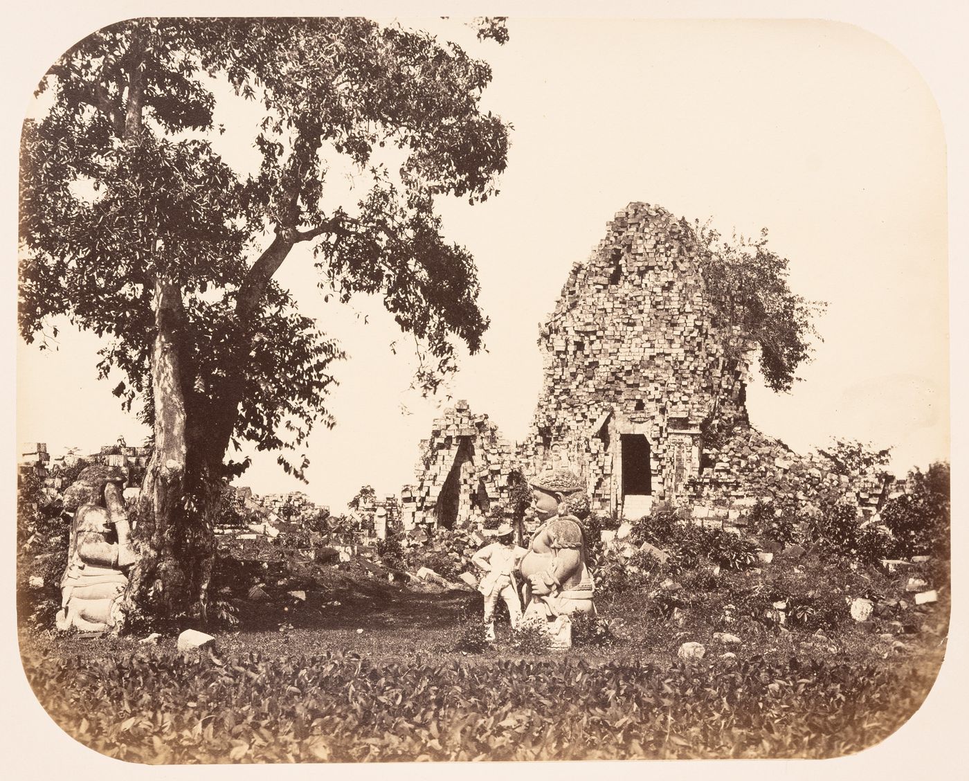 View of the ruins of stupas showing statues of Gupolo and a man, Candi Sewu, near Prambanan, Dutch East Indies (now Indonesia)