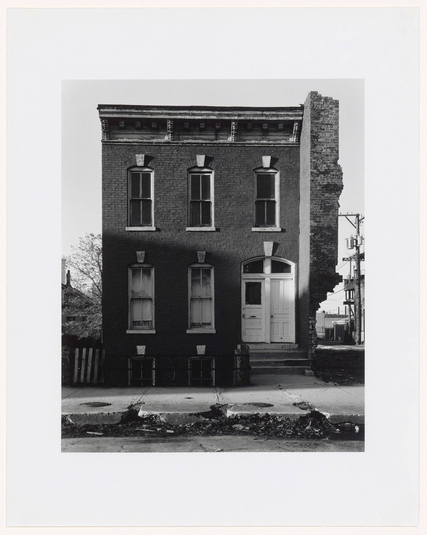 View of a house with remnants of a building on the left and a deteriorated sidewalk in the foreground, 749 Blackhawk Street, Chicago, Illinois, United States