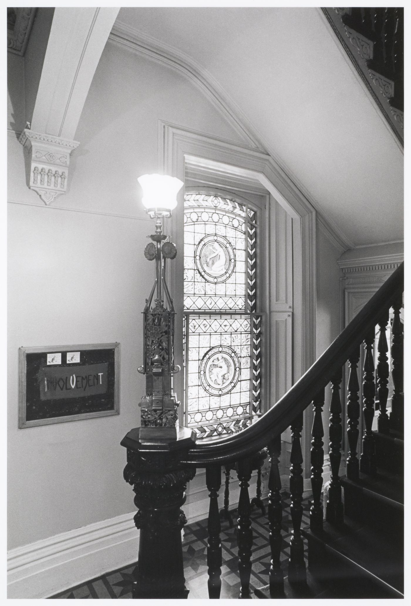 Interior view of the original carved wooden stairs and a stained glass window in the west part of Shaughnessy House, Montréal, Québec