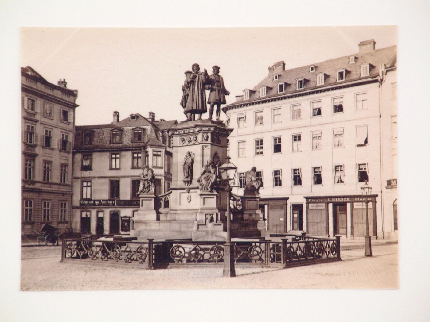 View of a monument to Gutenberg, Fust and Schöffer in a town [?] square with stores and apartment houses in the background, Germany