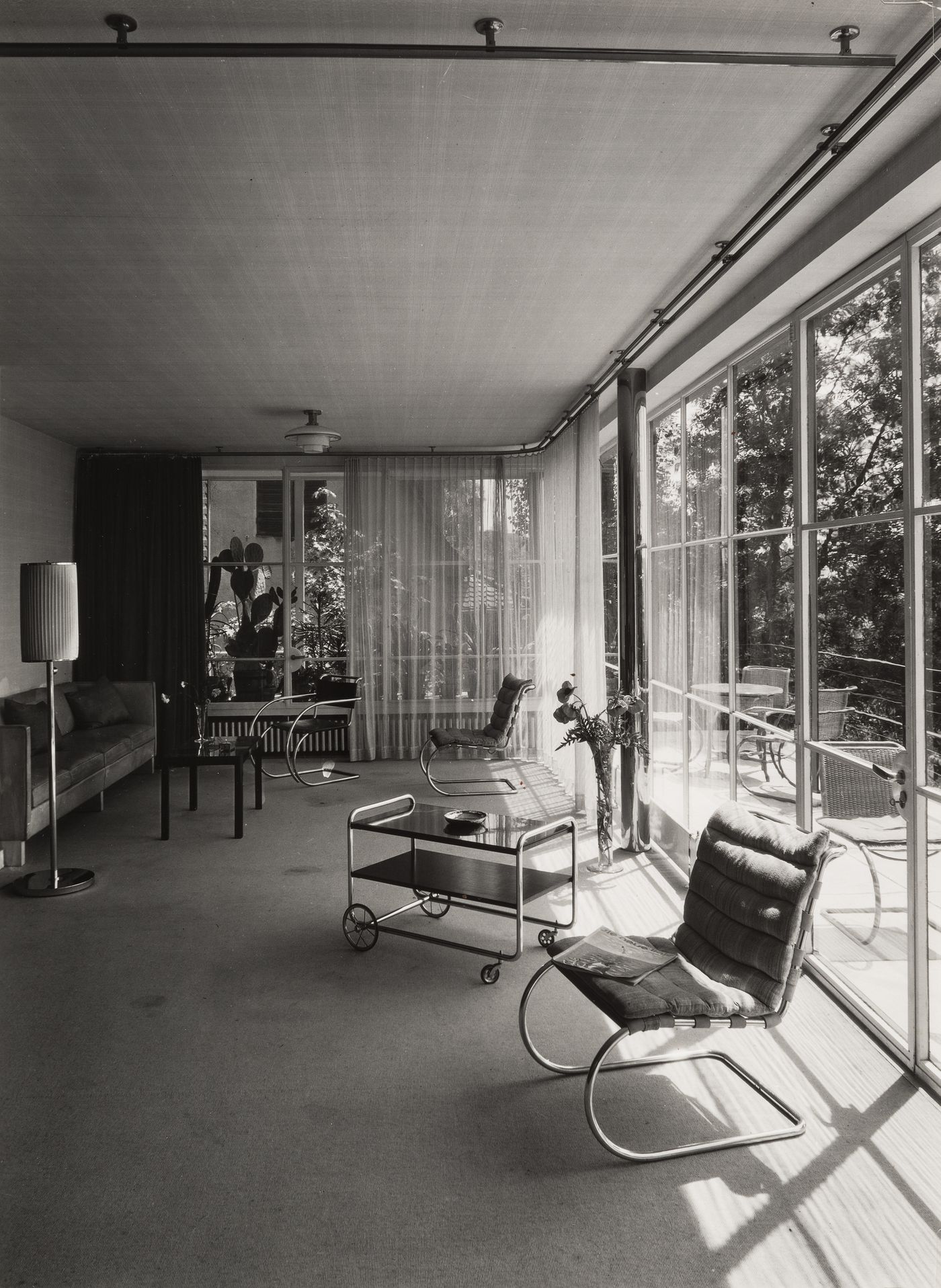 Interior, living room with tubular steel frame chairs and wheeled cart, patio visible beyond picture window