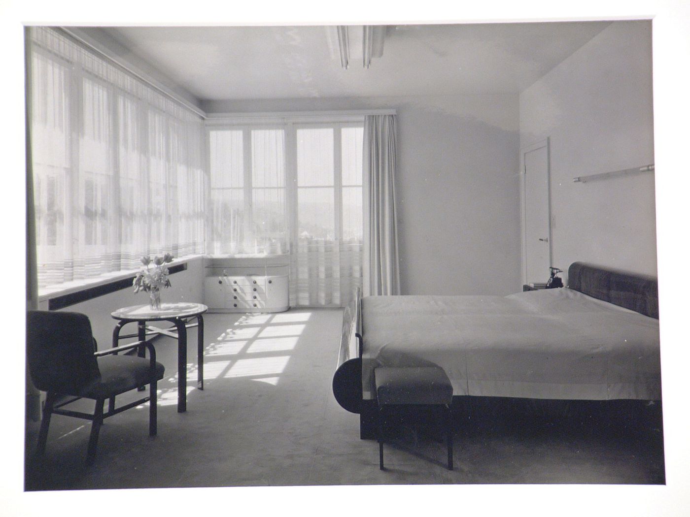 Interior of bedroom with large windows, and vase of tulips on small table, Germany