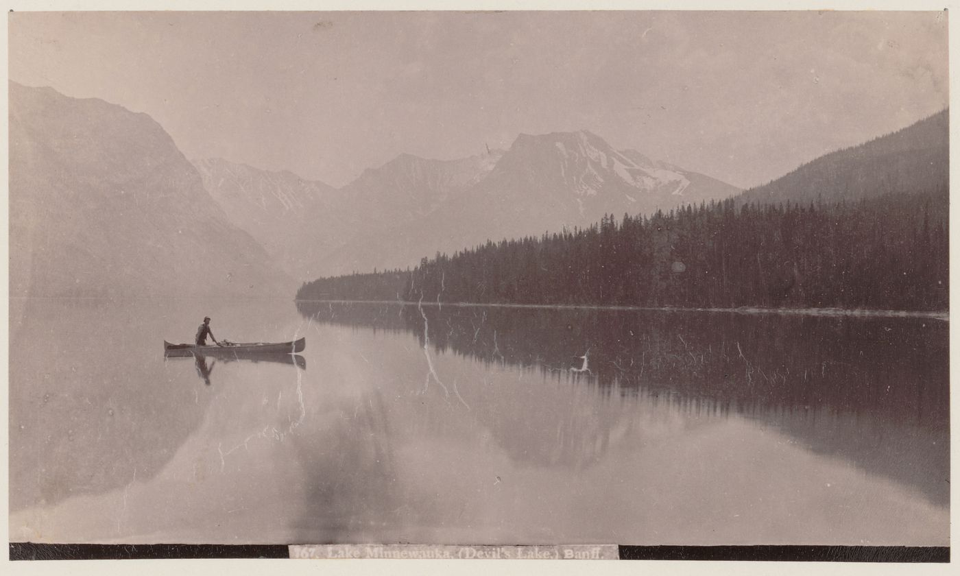 View of Lake Minnewanka (Devil's Lake) with a canoeist in the foreground and mountains in the background, Banff, Alberta