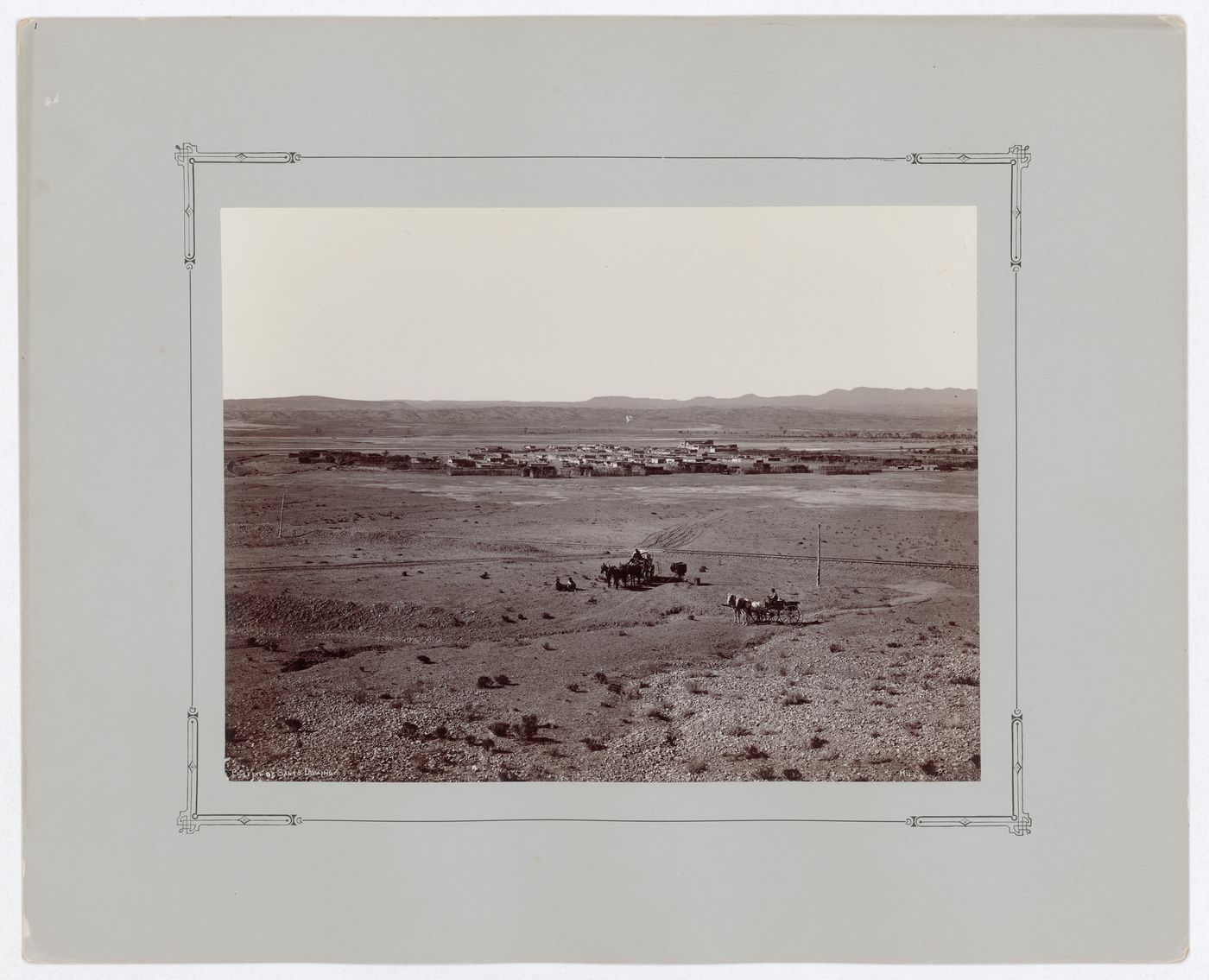 Distant view of Kewa Pueblo (Santo Domingo Pueblo) showing fenced cultivated plots of land with railway tracks and horse-drawn carriages in the foreground, New Mexico, United States