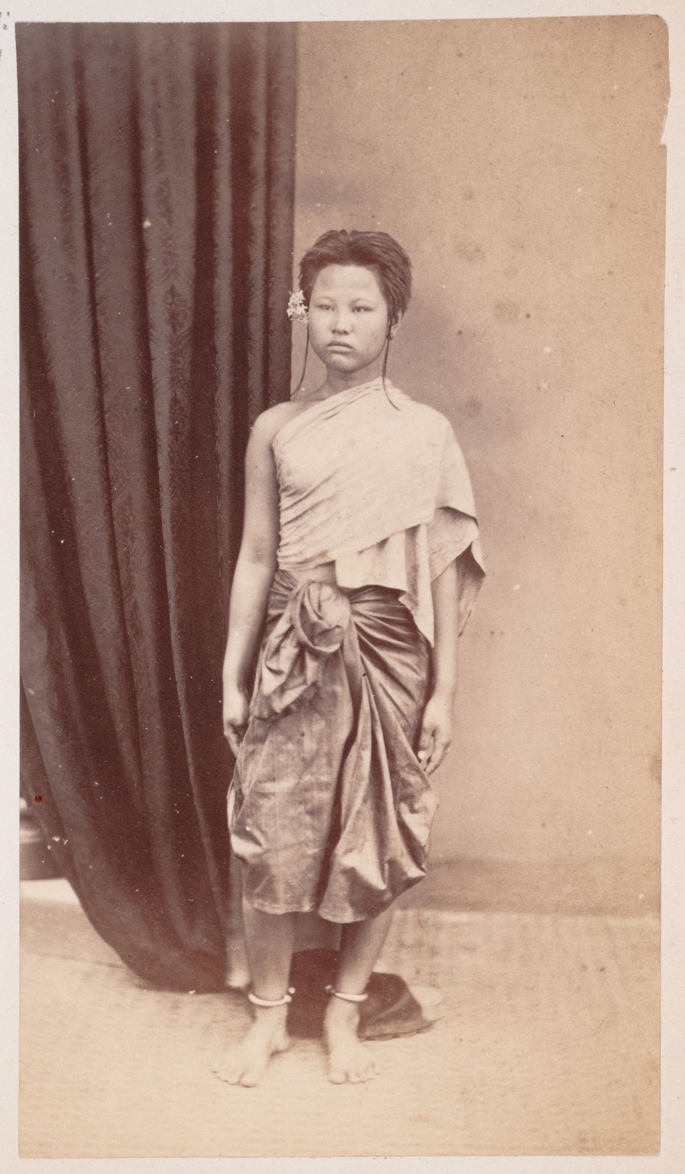 Portrait of a woman standing beside a curtain, probably in Cambodia