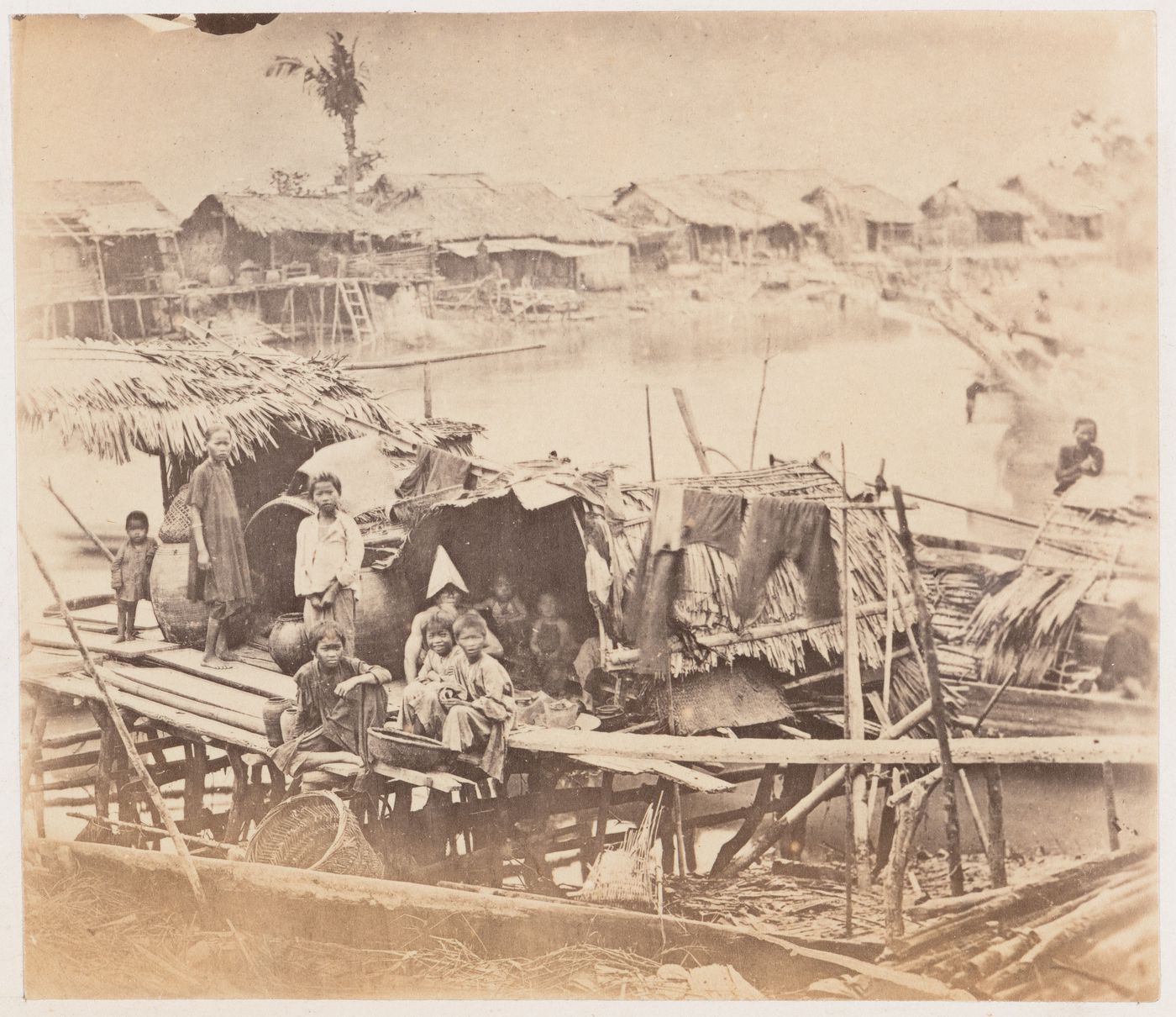 View of people on a wharf showing stilt houses, sampans and a river, Cholon (now Cho Lon), Cochin China (now in Vietnam)