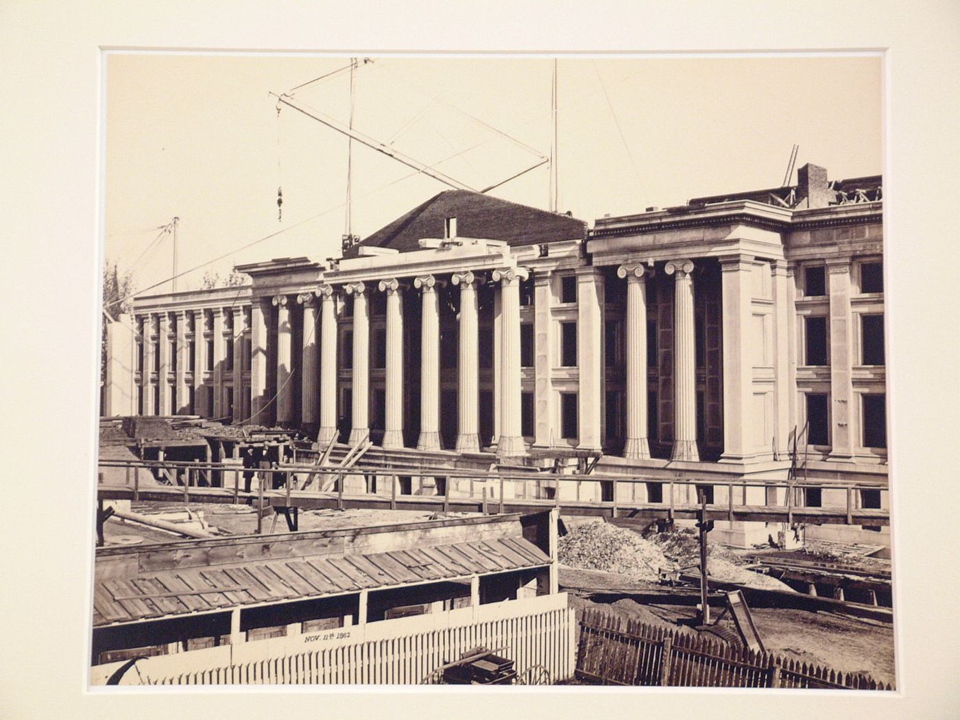 Treasury Building under contruction: Two figures on surrounding walkway, crane on roof, Washington, District of Columbia