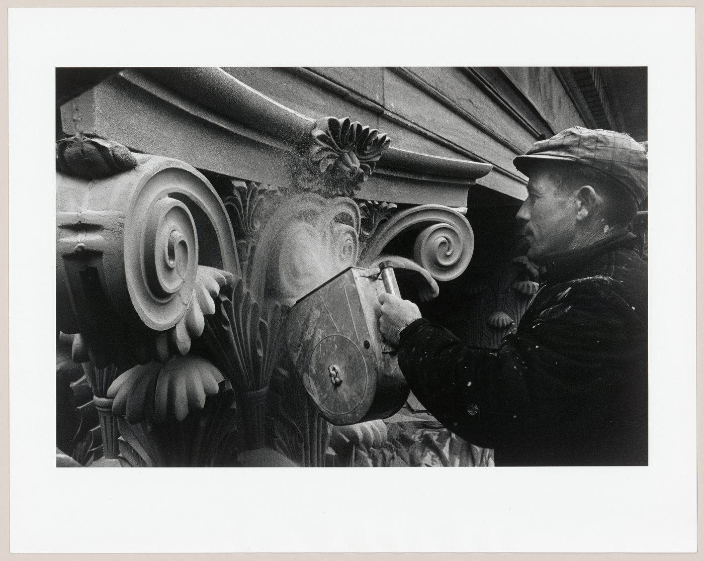 View of a worker dusting the exterior surface an aluminium capital with silica sand during the restoration of the Corinthian capitals of the principal façade of the Head Office of the Bank of Montréal, 119 rue Saint-Jacques, Montréal, Québec