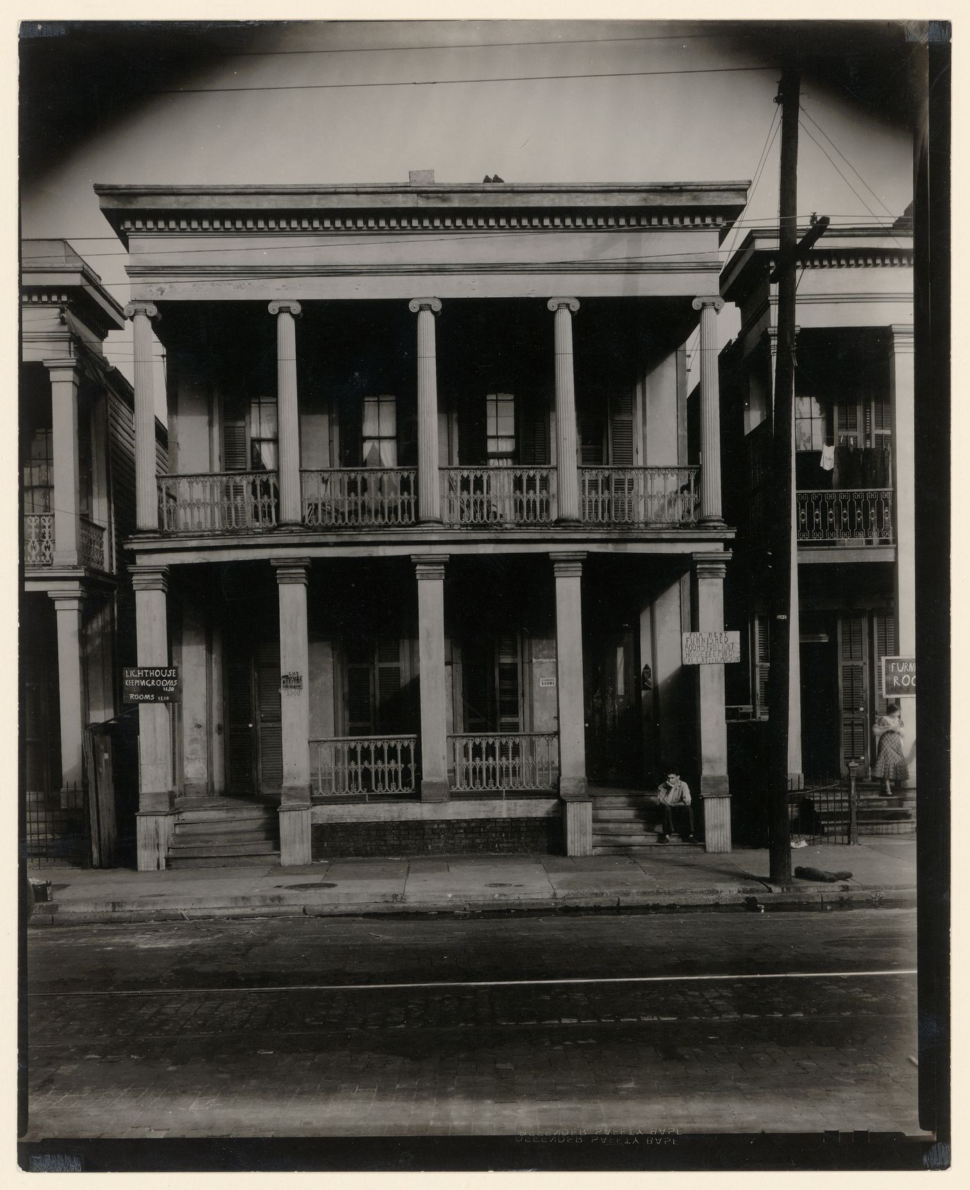 Boarding house: front view, man seated on steps, two-story house, women standing on step on the right, New Orleans