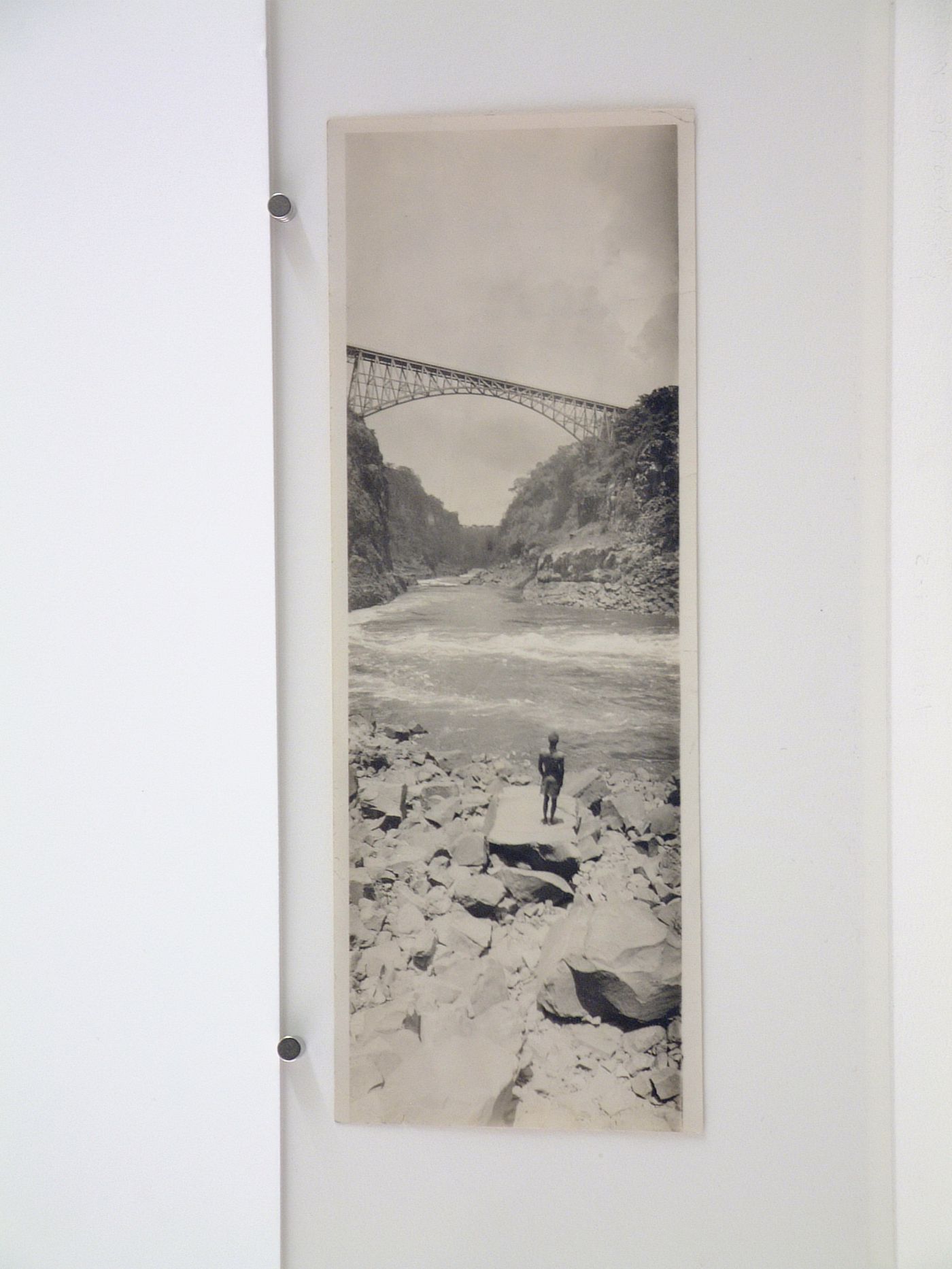 Vertical panoramic view of man standing on rock in front of Victoria Falls Bridge from below, Zambezi River, crossing the border between Victoria Falls, Zimbabwe and Livingstone, Zambia