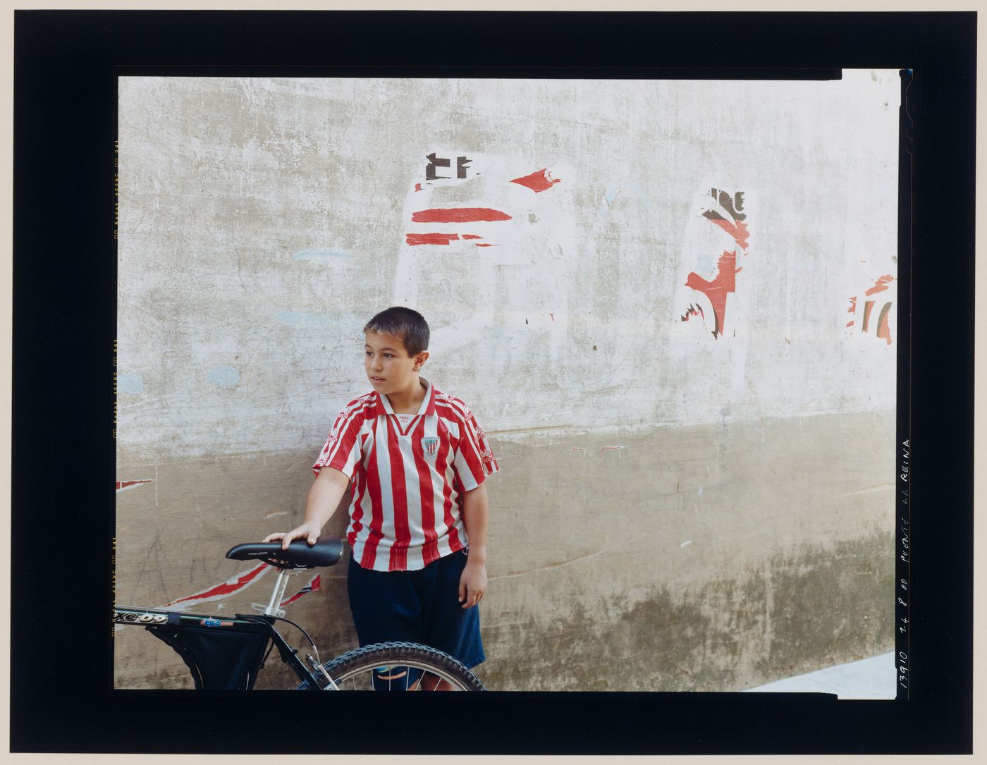 Portrait of a boy holding a bicycle and standing in front of a wall, Puente la Reina, Spain (from the series "In between cities")