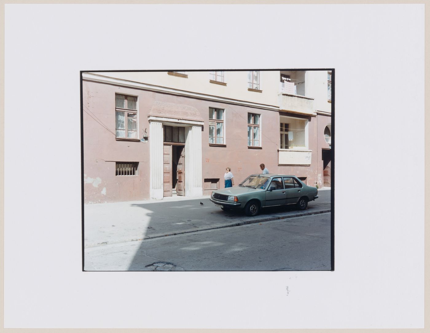 View of an apartment house showing a doorway, a street, a parked automobile and people, Kaliningrad, Kaliningradskaia oblast', Russia (from the series "In between cities")