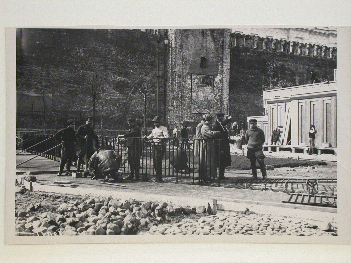 Partial view of the second wooden Lenin Mausoleum showing workers installing a metal fence in the foreground, Red Square, Moscow