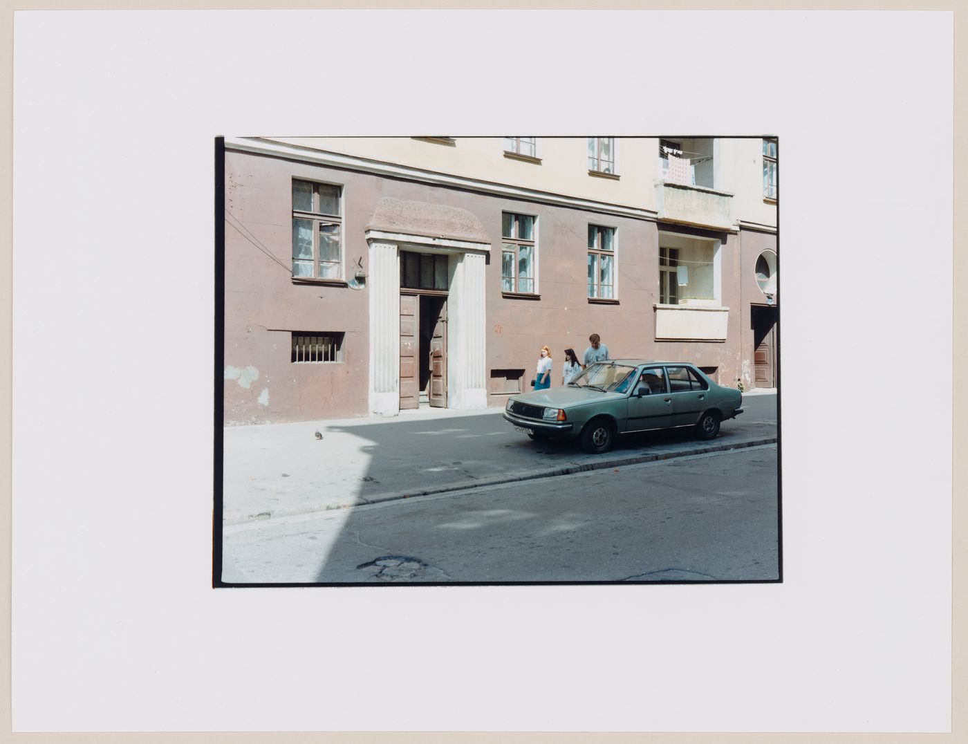 View of an apartment house showing a doorway, a street, a parked automobile and people, Kaliningrad, Kaliningradskaia oblast', Russia (from the series "In between cities")