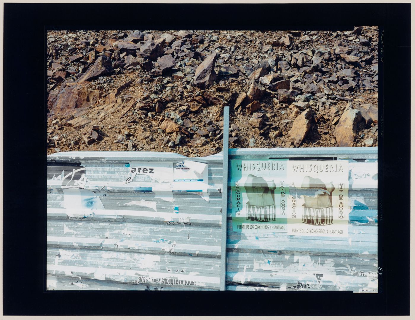 View of a metal guardrail bearing posters and a rocky slope, Santiago de Compostela, Spain (from the series "In between cities")