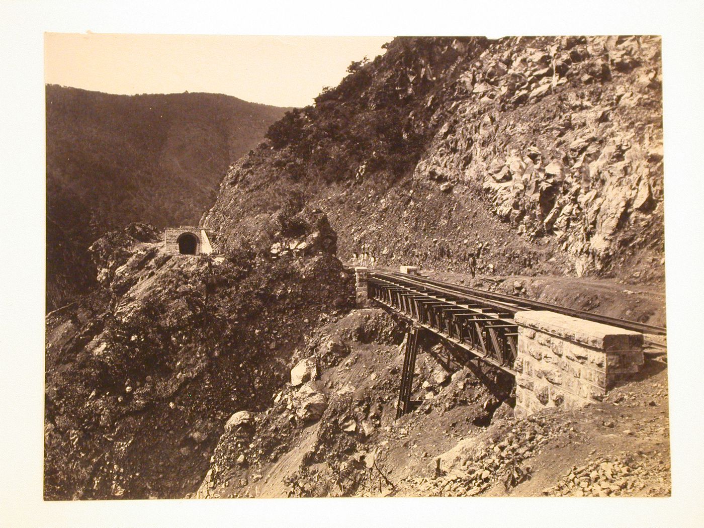View of a railroad bridge over the Barranca infiernilla, possibly in the Cumbres de Maltrata, with a group of men and a railroad tunnel entrance in the background, Veracruz-Llave, Mexico