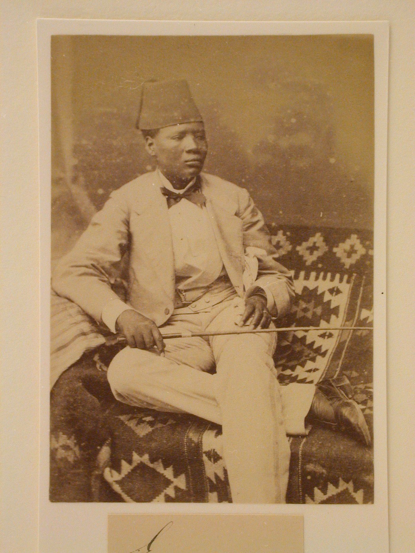 Man in suit and fez hat seated on blanket