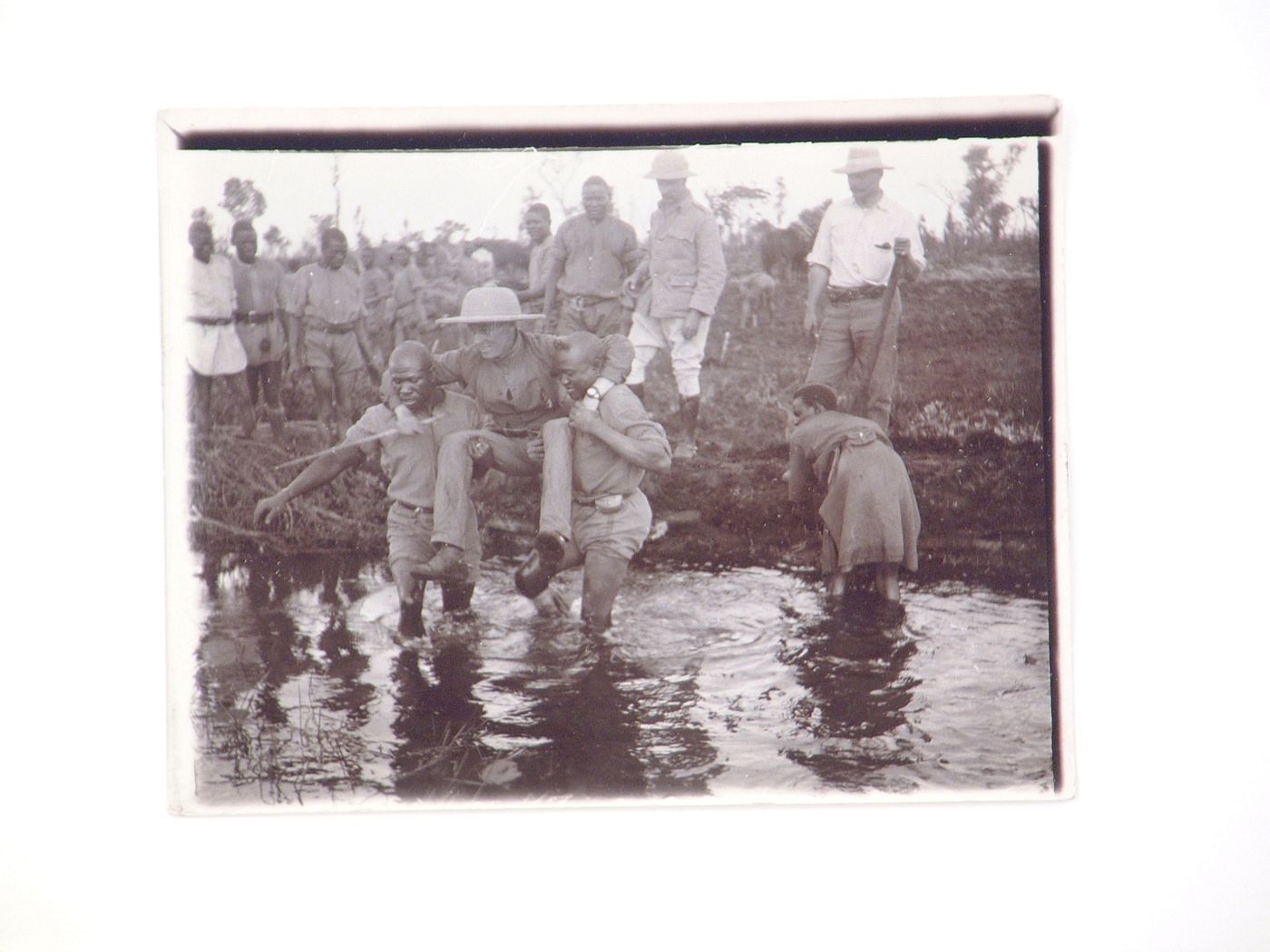 View of two men carrying a European man across a body of water, near Zambezi River