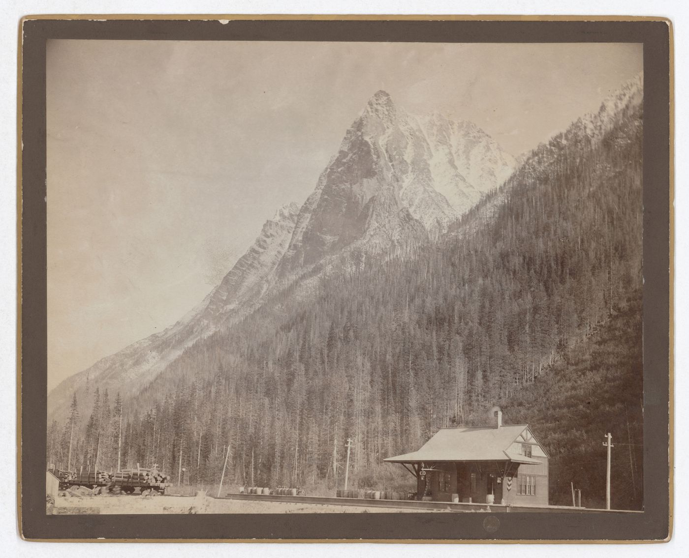 View of Mount Macdonald and Canadian Pacific Railway station with barrels and freight cars, Rogers Pass, British Columbia, Canada