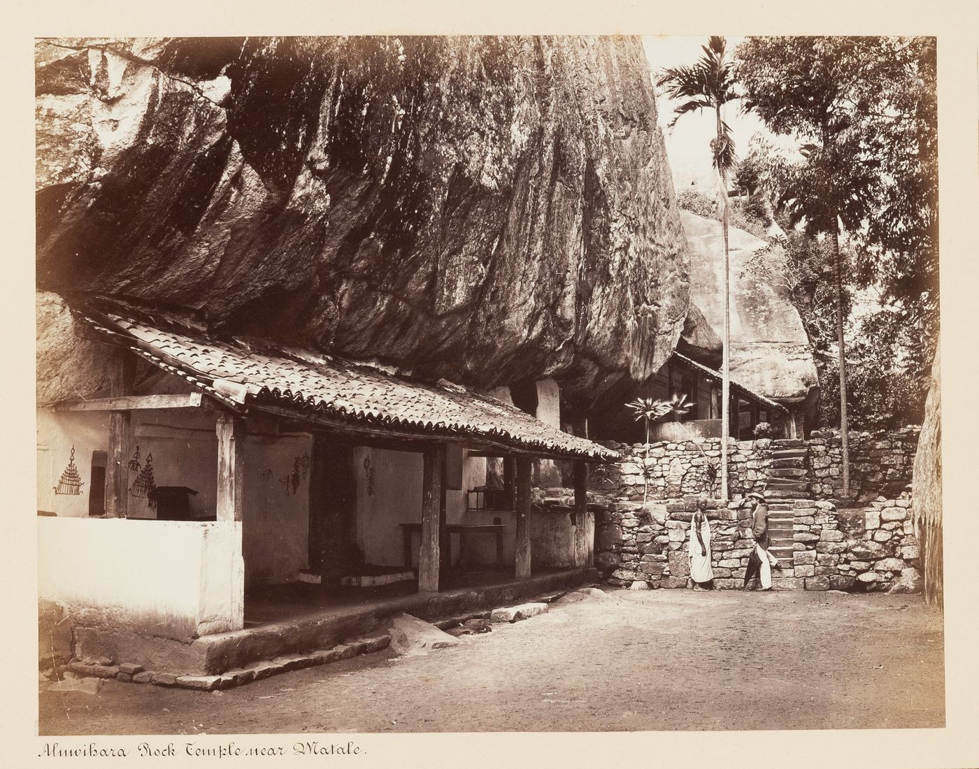 View of Aluwihare Rock Temple with a priest and government agent, Mr. Ross, on the right, Aluwihare, Ceylon (now Sri Lanka)