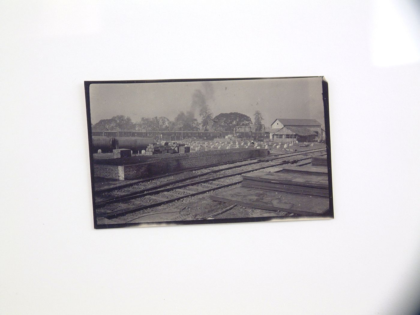 View of railway yard with building materials and train station in background, unknown location