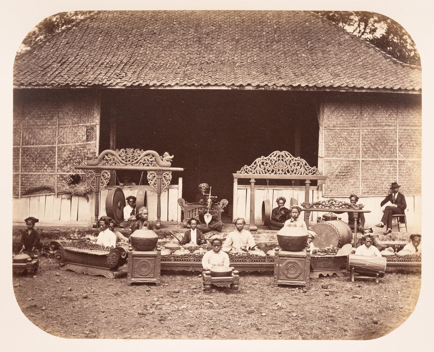 Group portrait of the musicians and instruments of the gamelan of the Regent of Bandong (now Bandung) showing the Regent's  palace, Bandong (now Bandung), Dutch East Indies (now Indonesia)