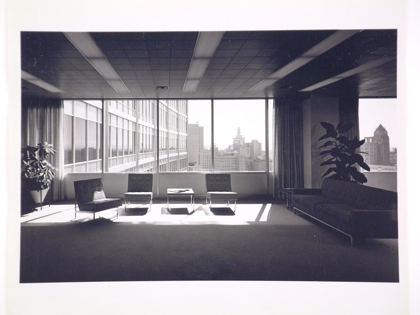 Interior view of an executive lounge in the Kaiser Center office building showing furniture in the foreground and buildings in the background, Oakland, California