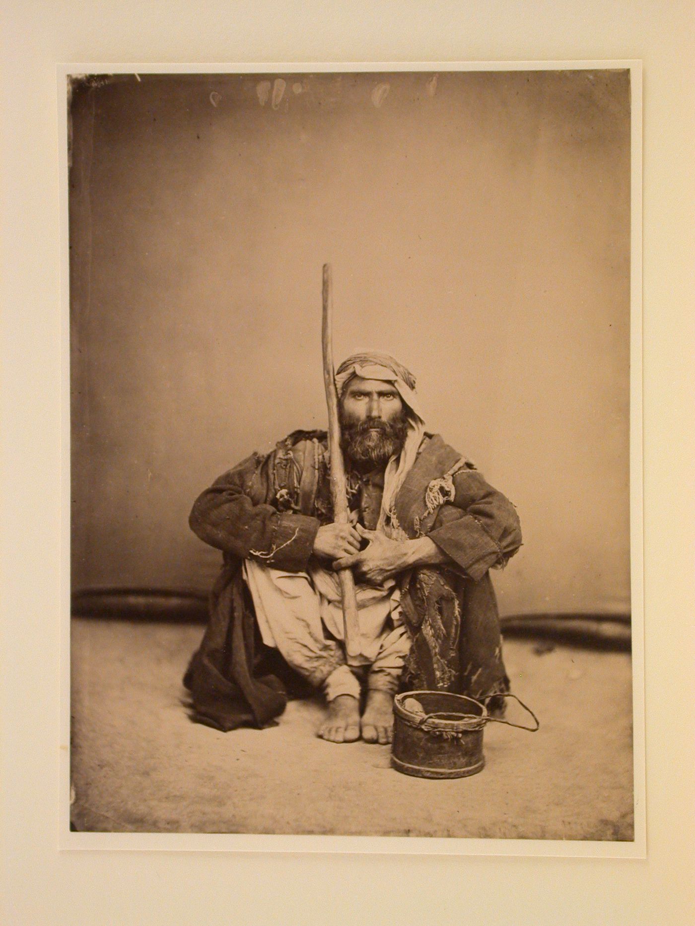 Studio portrait of a man sitting holding a stick with bucket in the foreground, Eastern Mediterranean