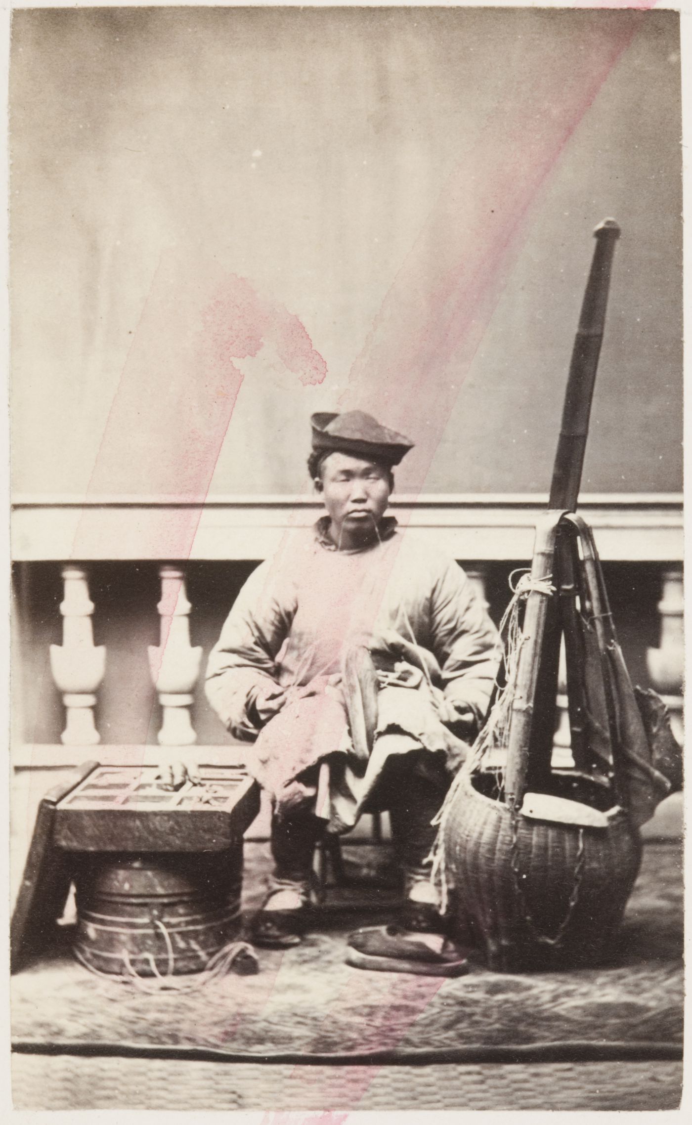 Portrait of a Chinese cobbler (peddler) repairing shoes, with his equipment beside him
