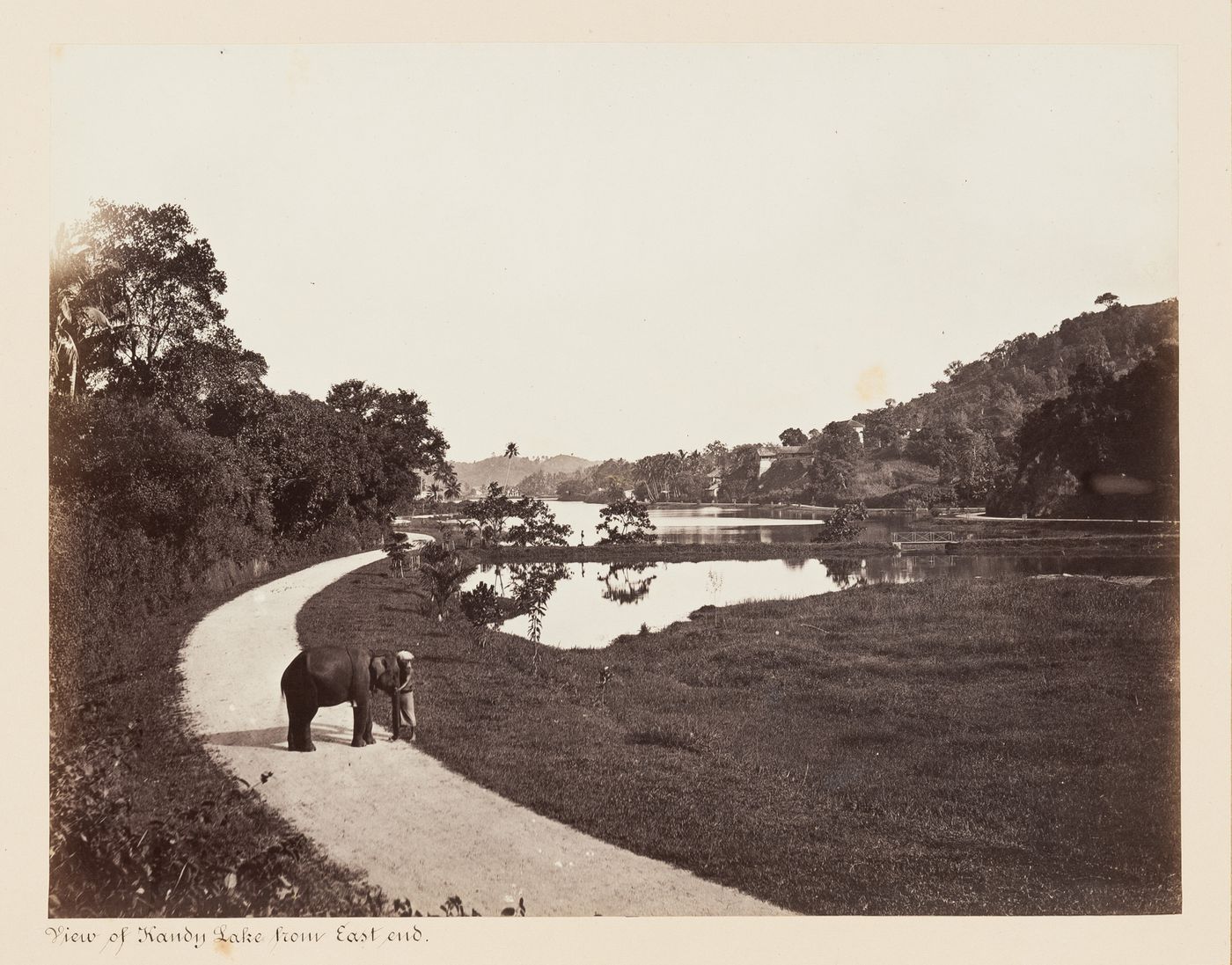 View of Kandy Lake from the east end with a man and an elephant on the left, Kandy, Ceylon (now Sri Lanka)