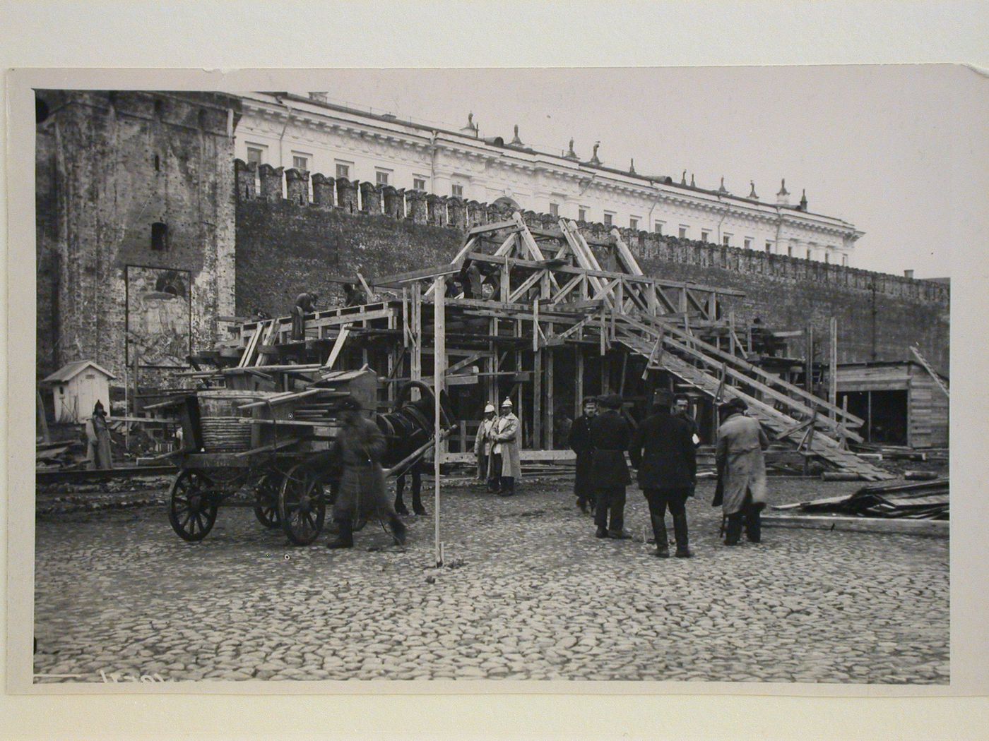 View of the second wooden Lenin Mausoleum under construction with workers, guards and a horse-driven loaded wagon in the foreground, Red Square, Moscow