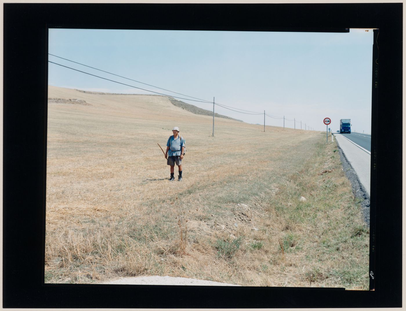 Portrait of a man standing in a field showing utility poles and a road, Burgos, Spain (from the series "In between cities")