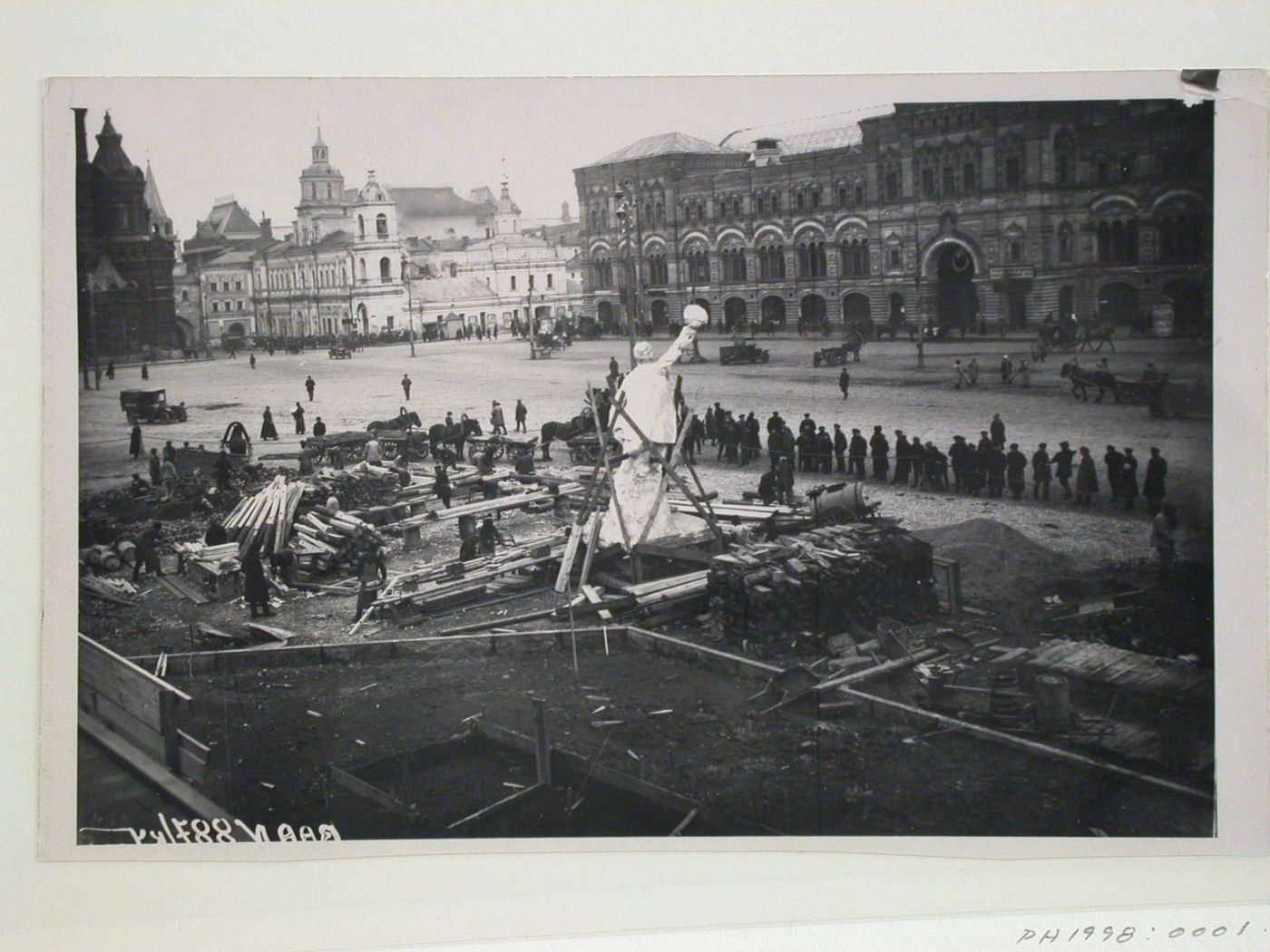 View of the construction site of the second wooden Lenin Mausoleum before work commenced, showing construction materials, a monument, and the Upper Shopping Arcades, Red Square, Moscow