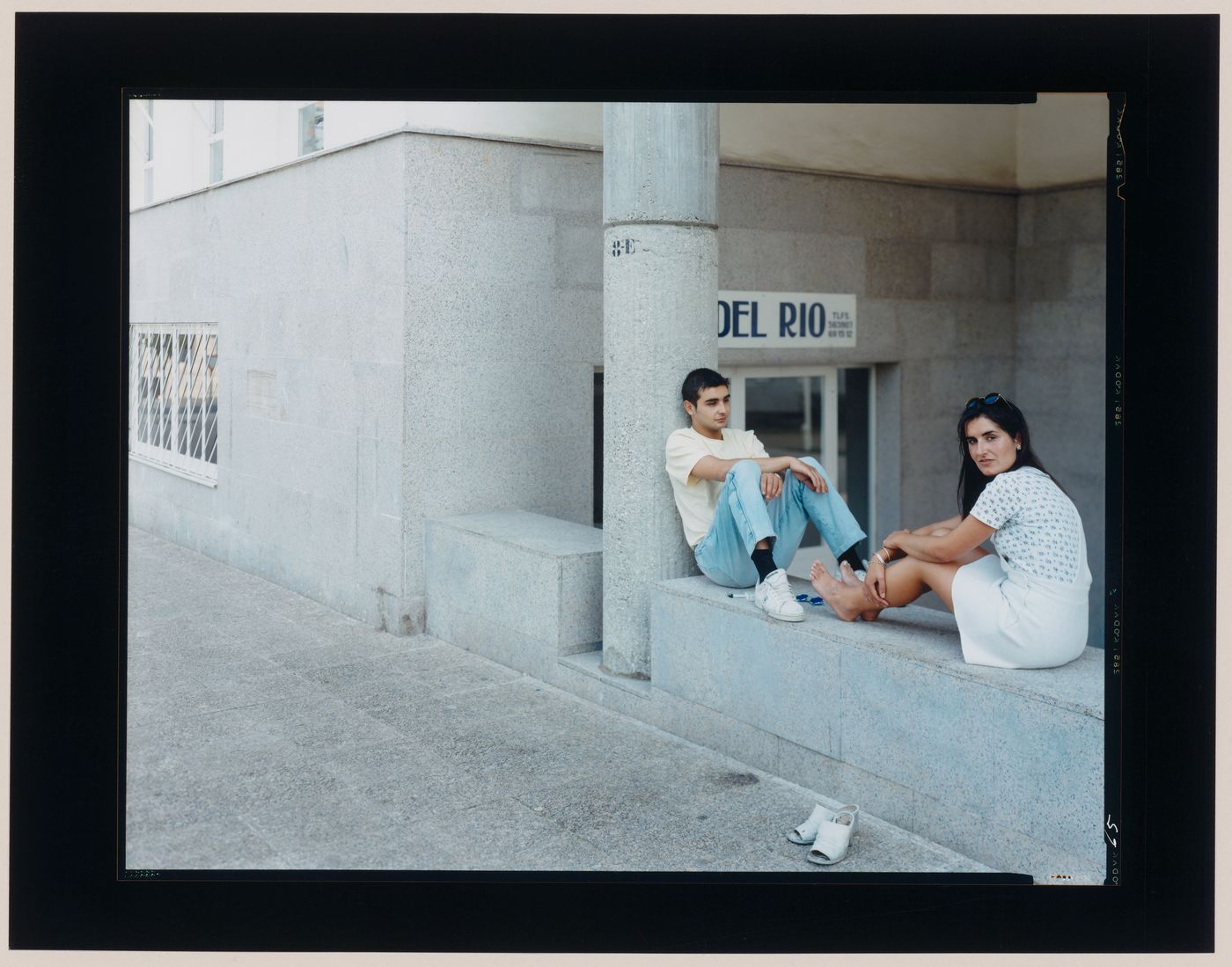 Group portrait of a woman and a man sitting on a wall by the entrance to a building, Santiago de Compostela, Spain (from the series "In between cities")