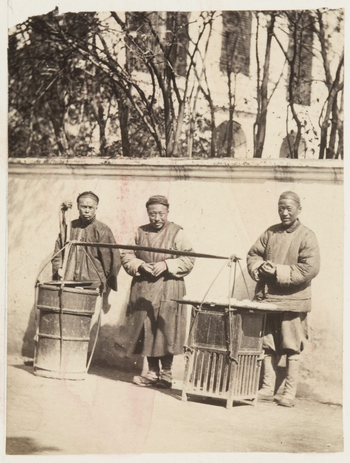 Portrait of a Chinese peddler and two cutomers ? standing outside a wall