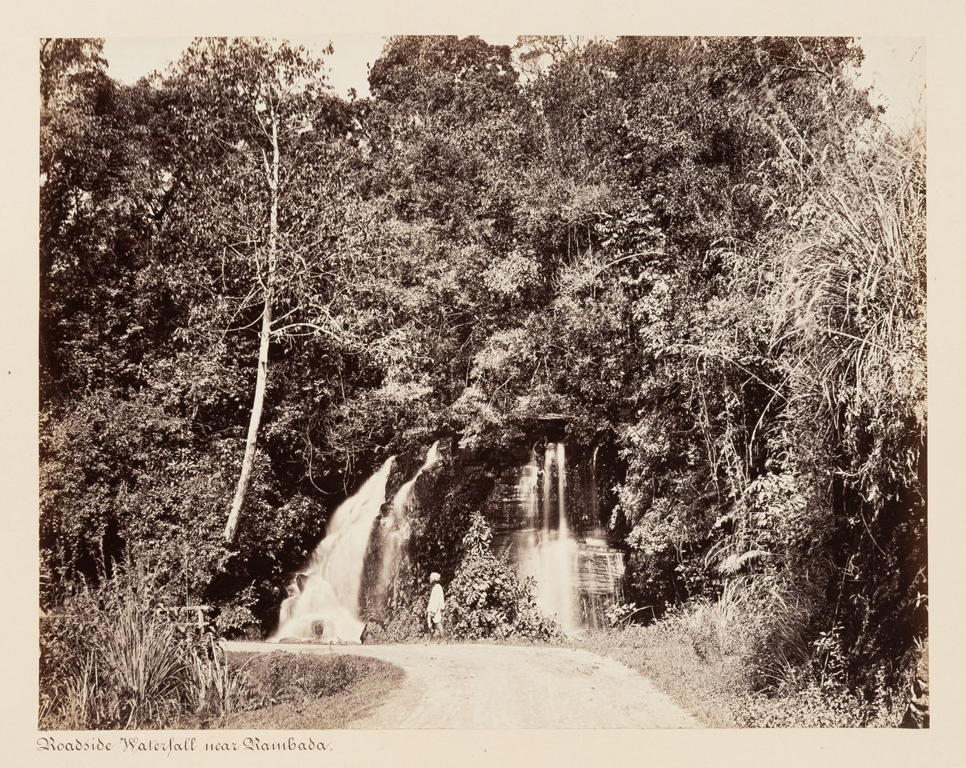 View of a waterfall with a road and man in the foreground, near Ramboda, Ceylon (now Sri Lanka)
