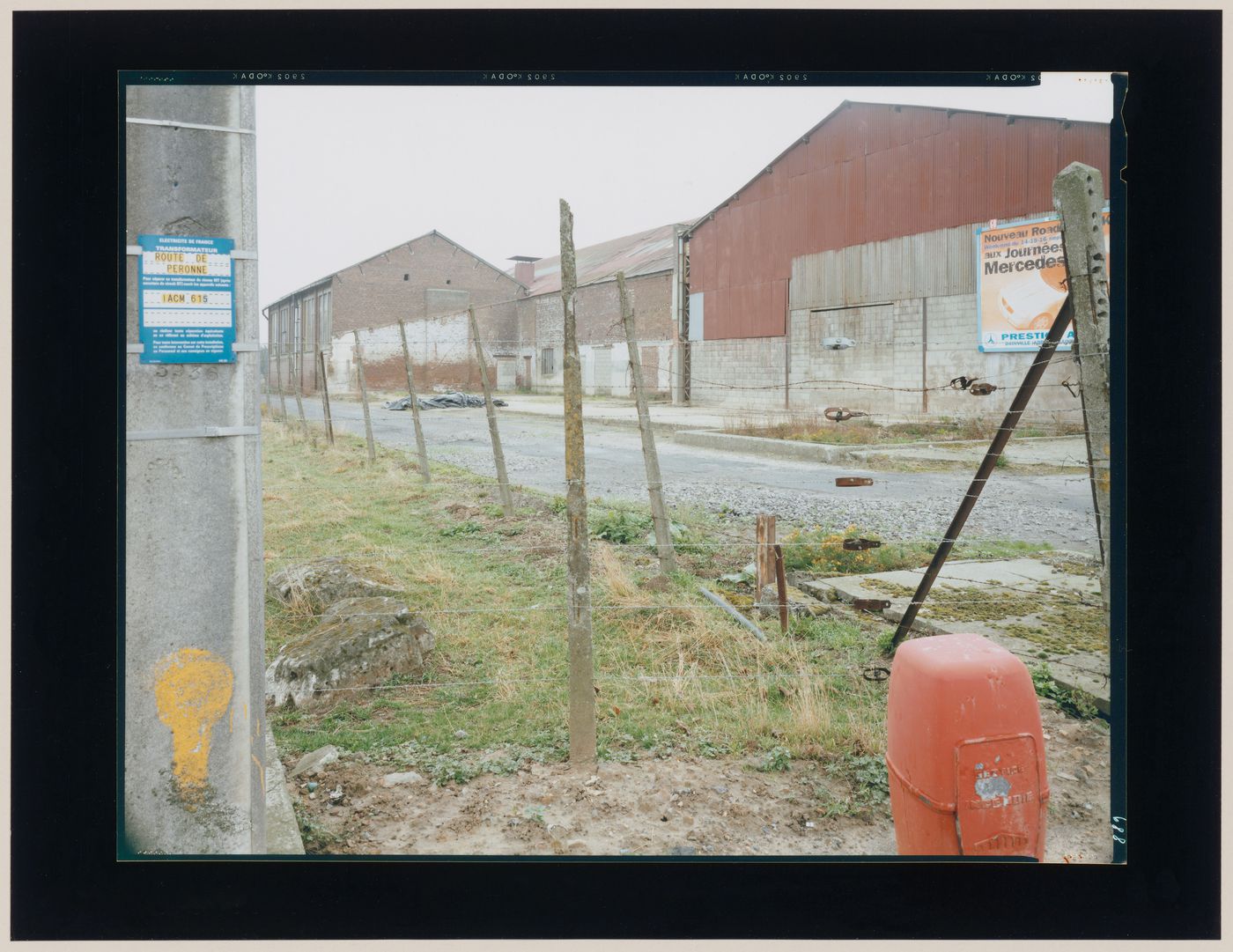 View of buildings, a lane and a fence showing a billboard, probably Dainville, near Arras, France