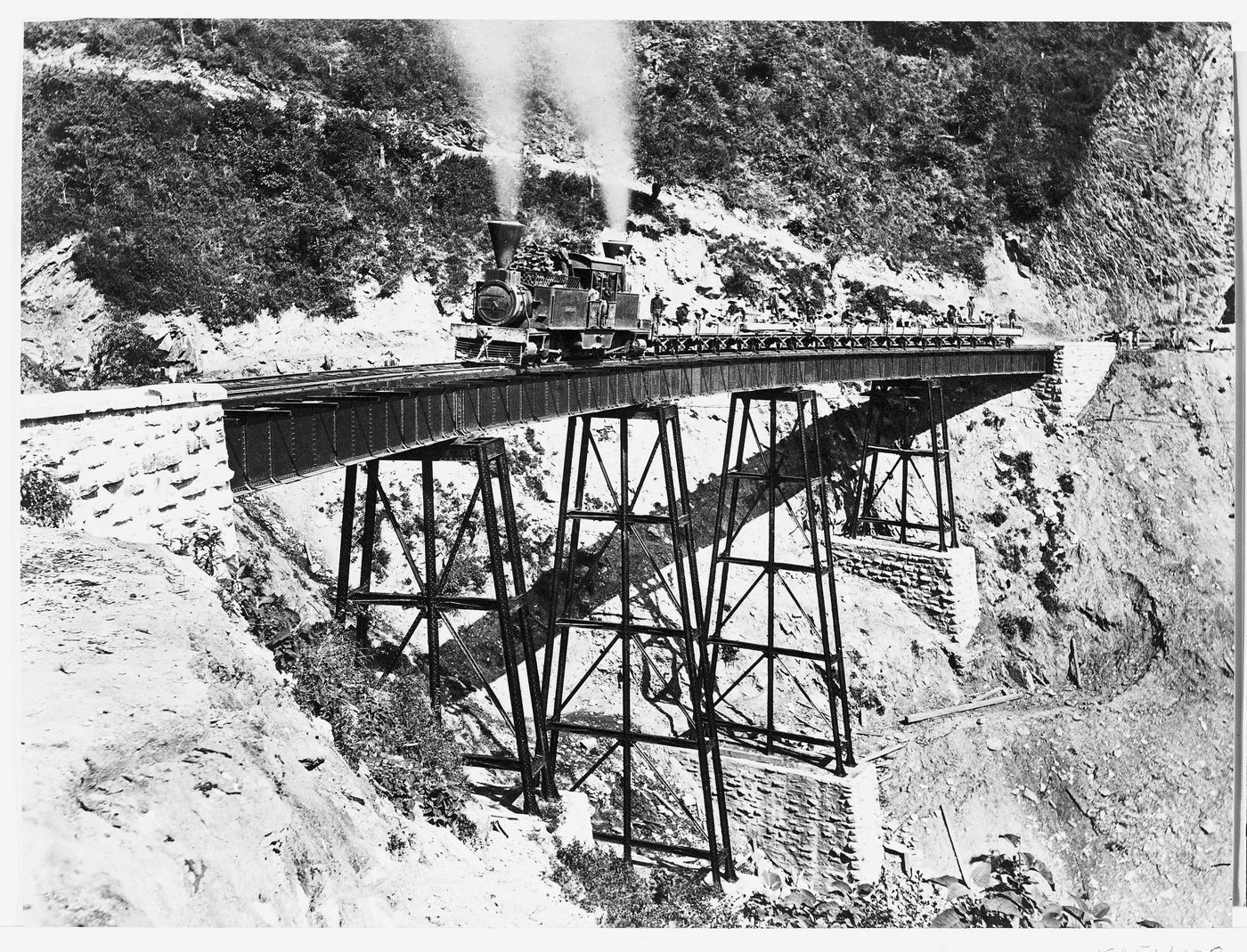 View of the Wimer railroad bridge in the Cumbres de Maltrata showing a locomotive and groups of men in railway wagons, Veracruz-Llave, Mexico