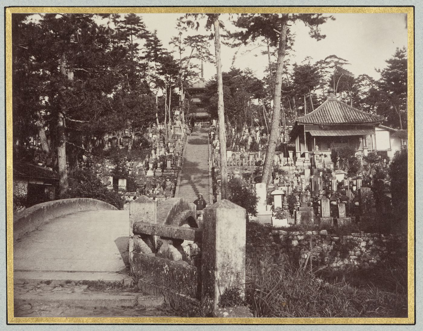 View of a cemetery showing tombstones, a stone bridge, stairs, and a building with a pagoda in the background, Kyoto, Japan