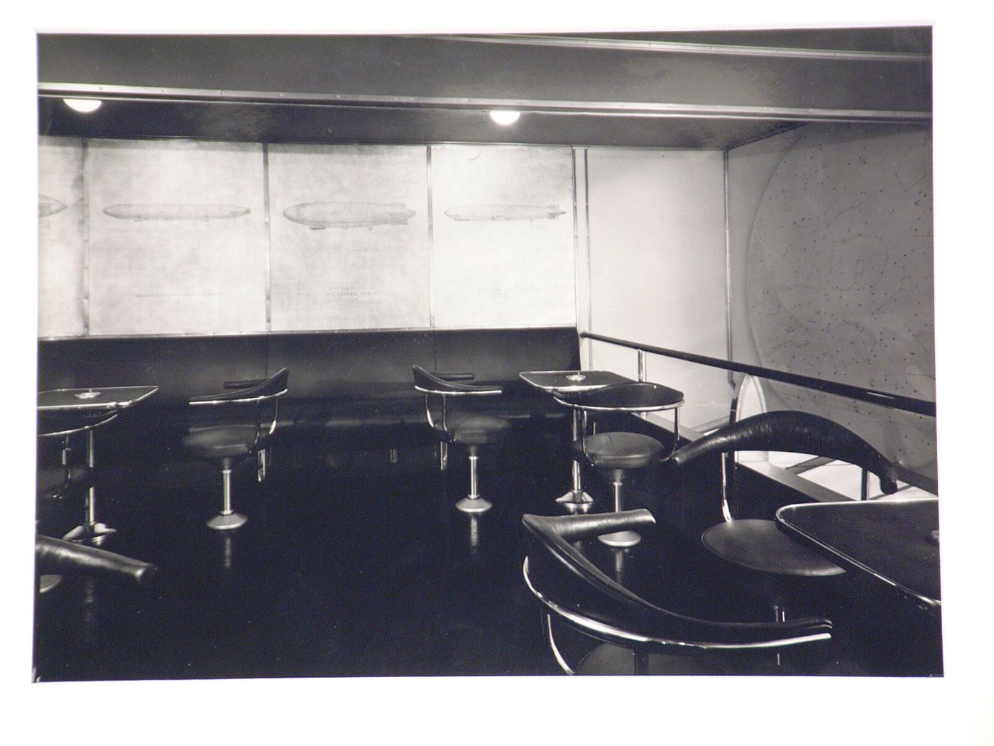 Interior of Zeppelin, with small tables and chairs, drawing of other Zeppelins and a star chart on the walls