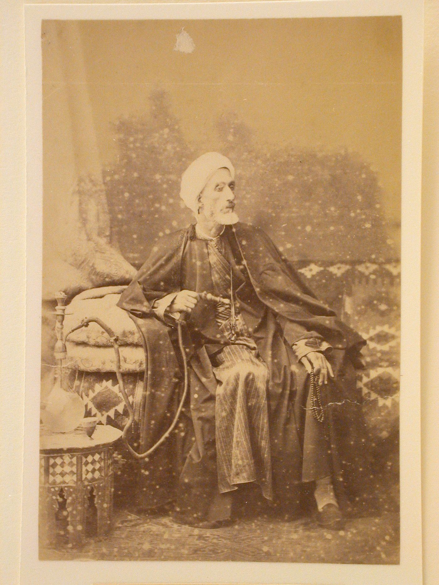 Studio portrait of a man with white beard sitting on bench, smoking hookah, Egypt