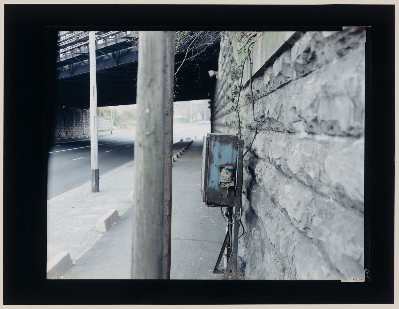 View of a road under an overpass showing a stone wall, posts and a call box, Saint-Denis, France (from the series "In between cities")