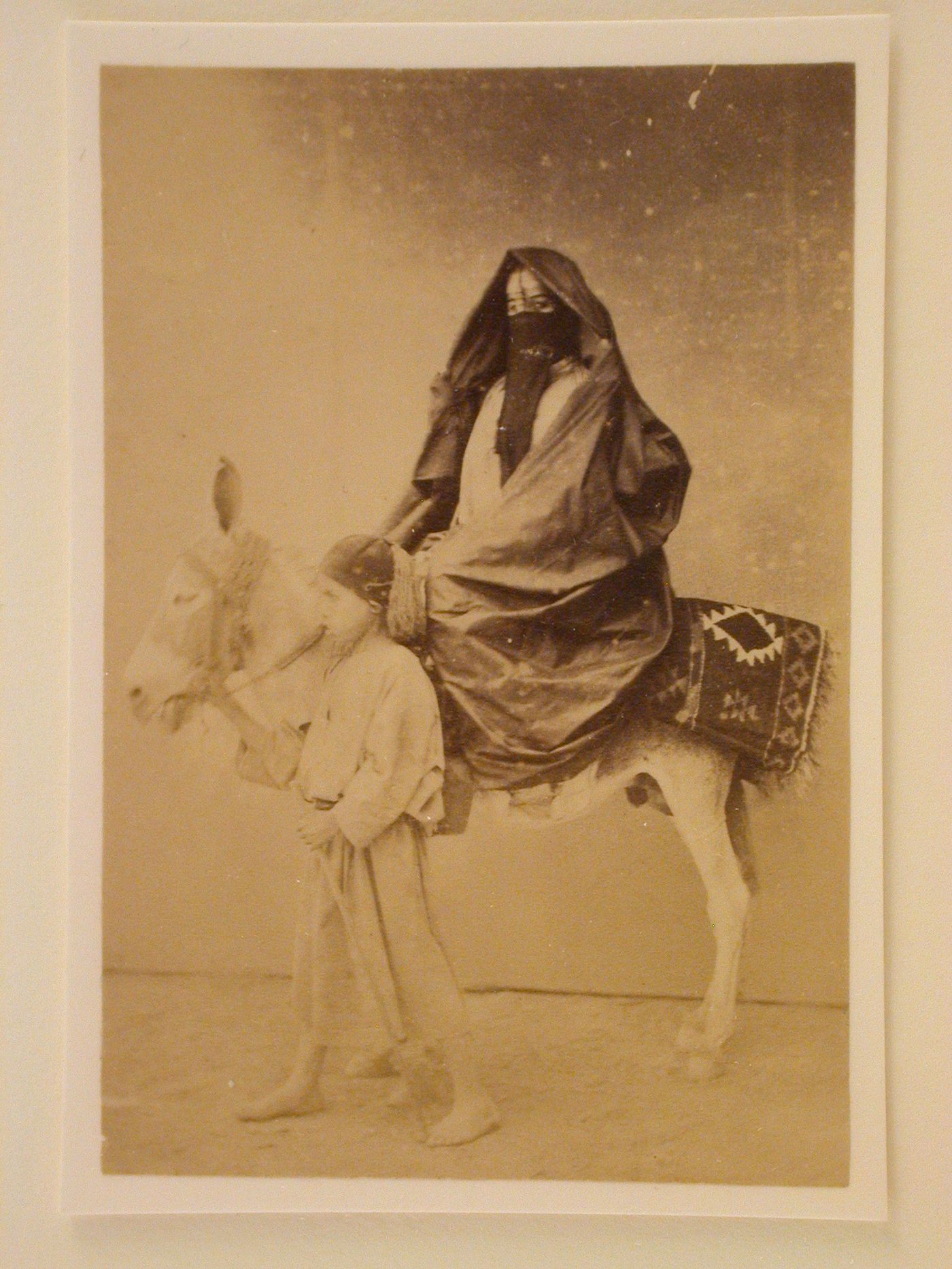 Veiled covered woman seated on a donkey led by a young boy