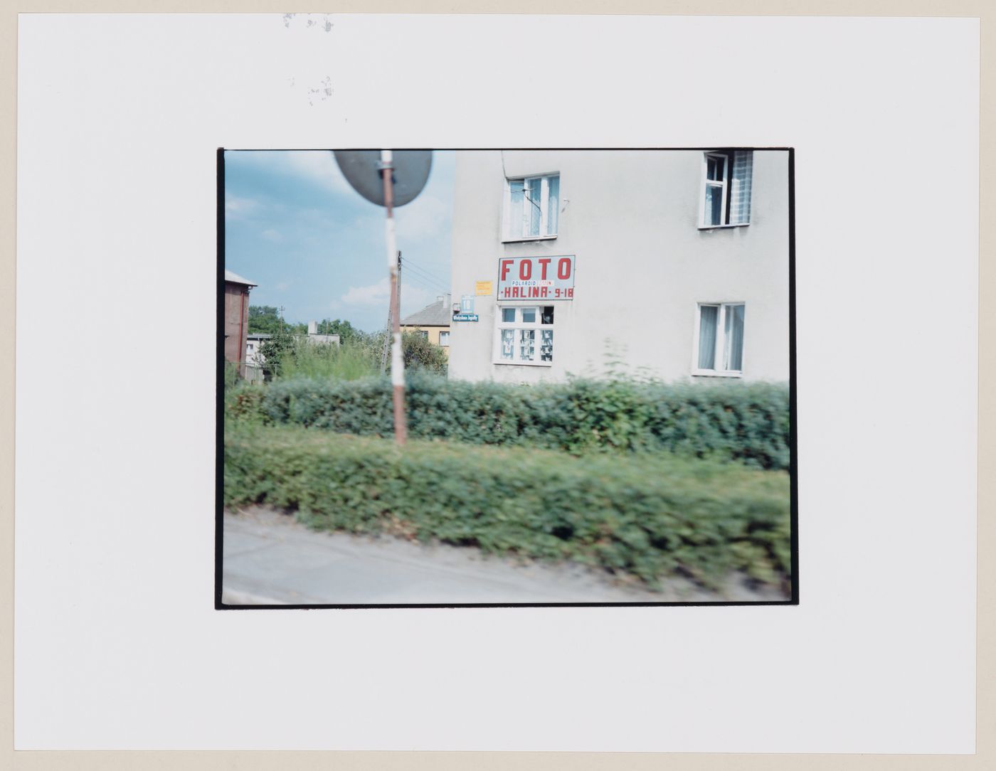 View of a building with a painted sign on the wall showing hedges in the foreground, Frombork, Poland (from the series "In between cities")