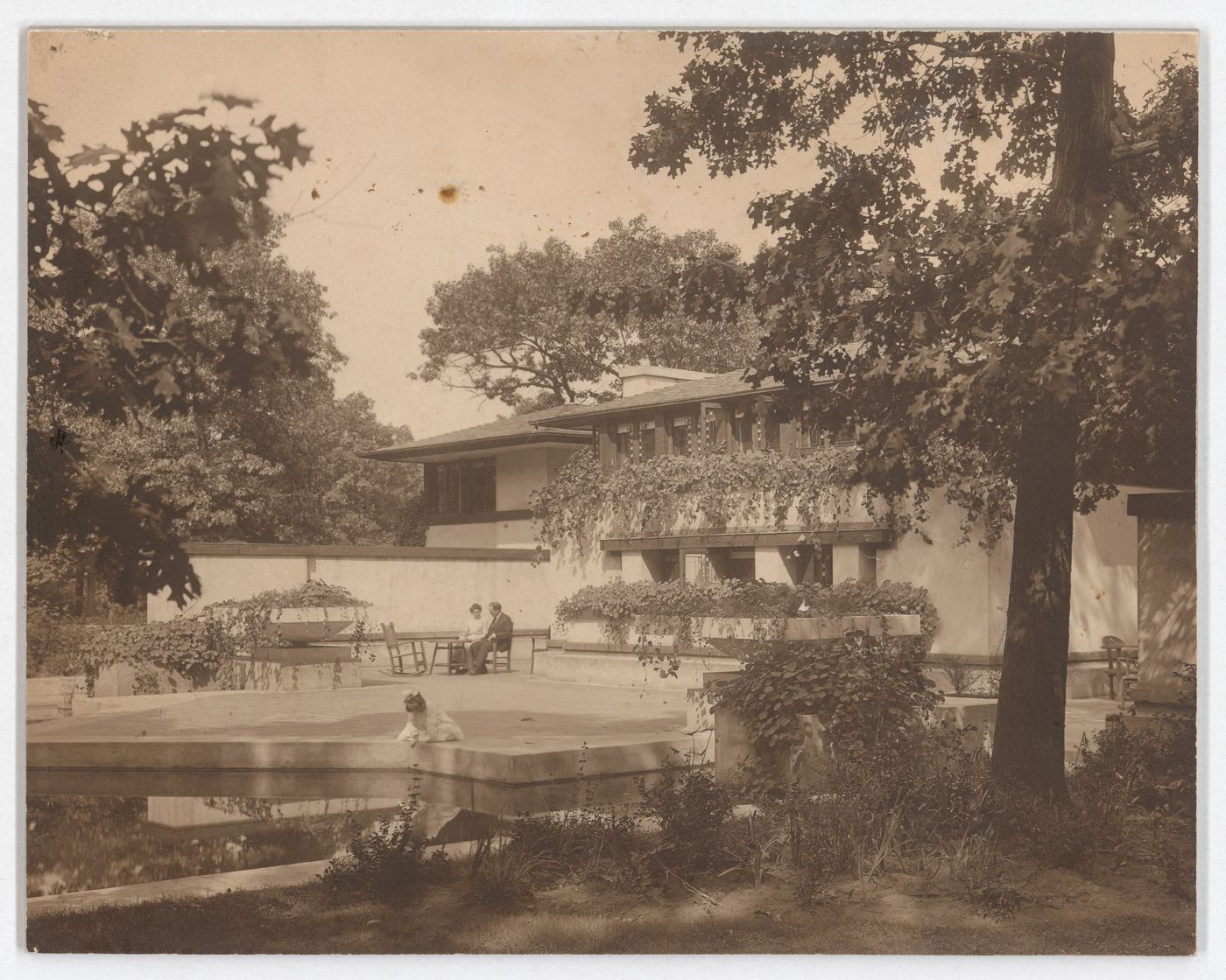 Exterior view of Coonley House showing Queene Ferry Coonley [?], Avery Coonley [?] and their daughter sitting by the pool, Riverside, Illinois