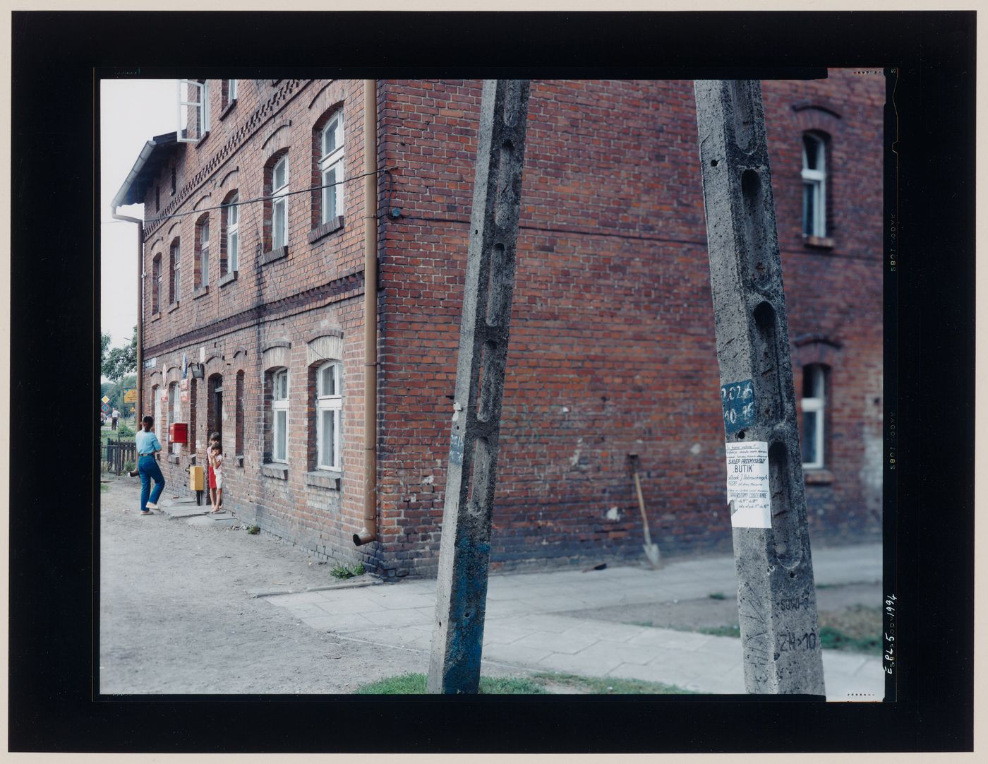 View of a brick building showing concrete posts in the foreground, Czarna Woda, Poland (from the series "In between cities")