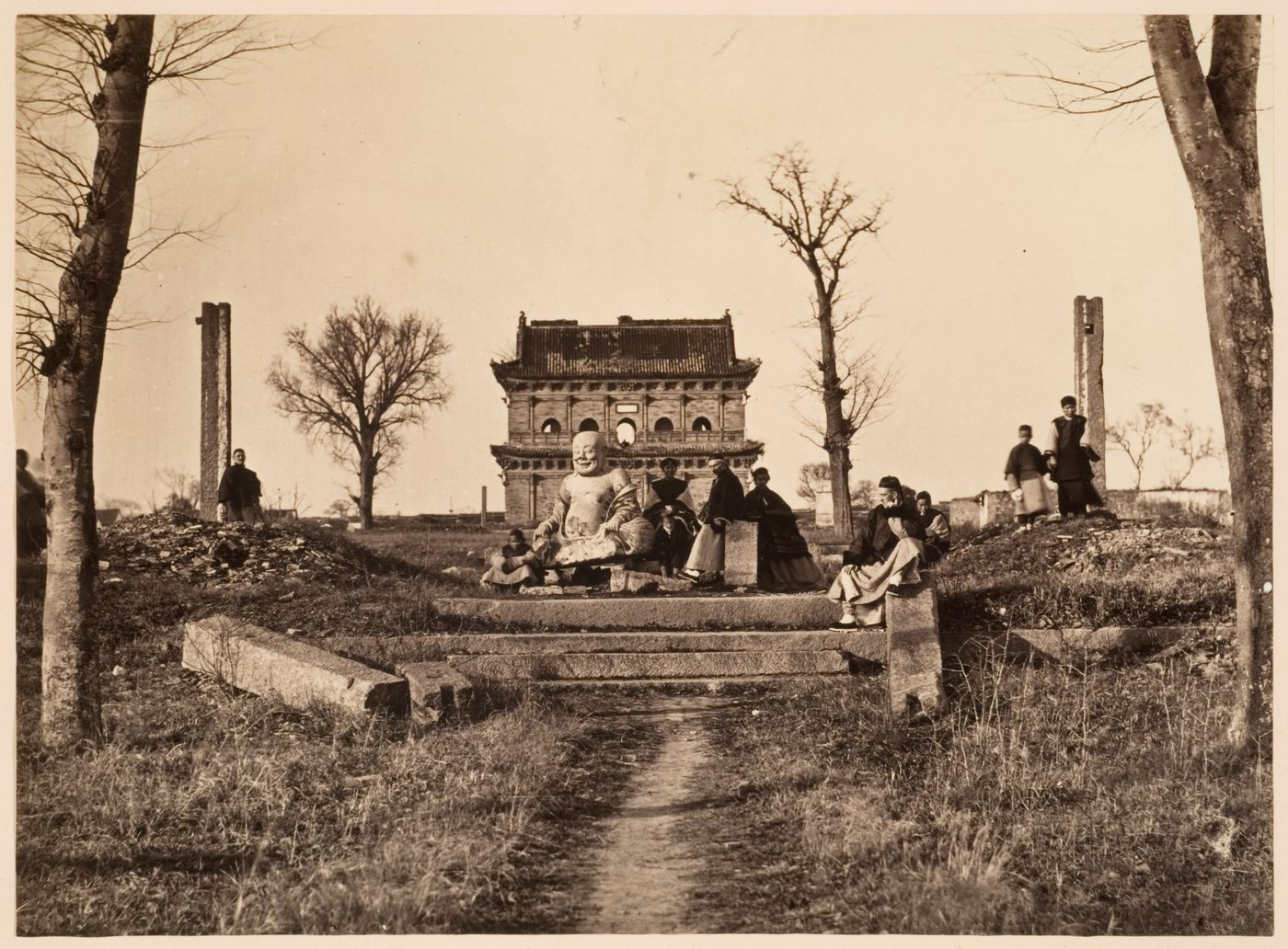 View of a group of people and a statue of Maitreya Buddha [Mi-le Fo] with the ruins of the Building for Buddhist Scripture in the background, K'ai-yuan [Kaiyuan] Temple, near Soochow (now Suzhou), China