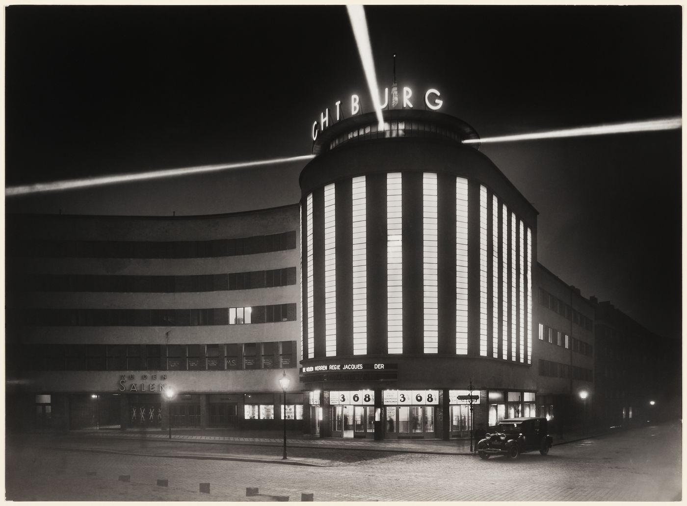 Night view of movie theater with light beacons near roof and large illuminated windows, Germany