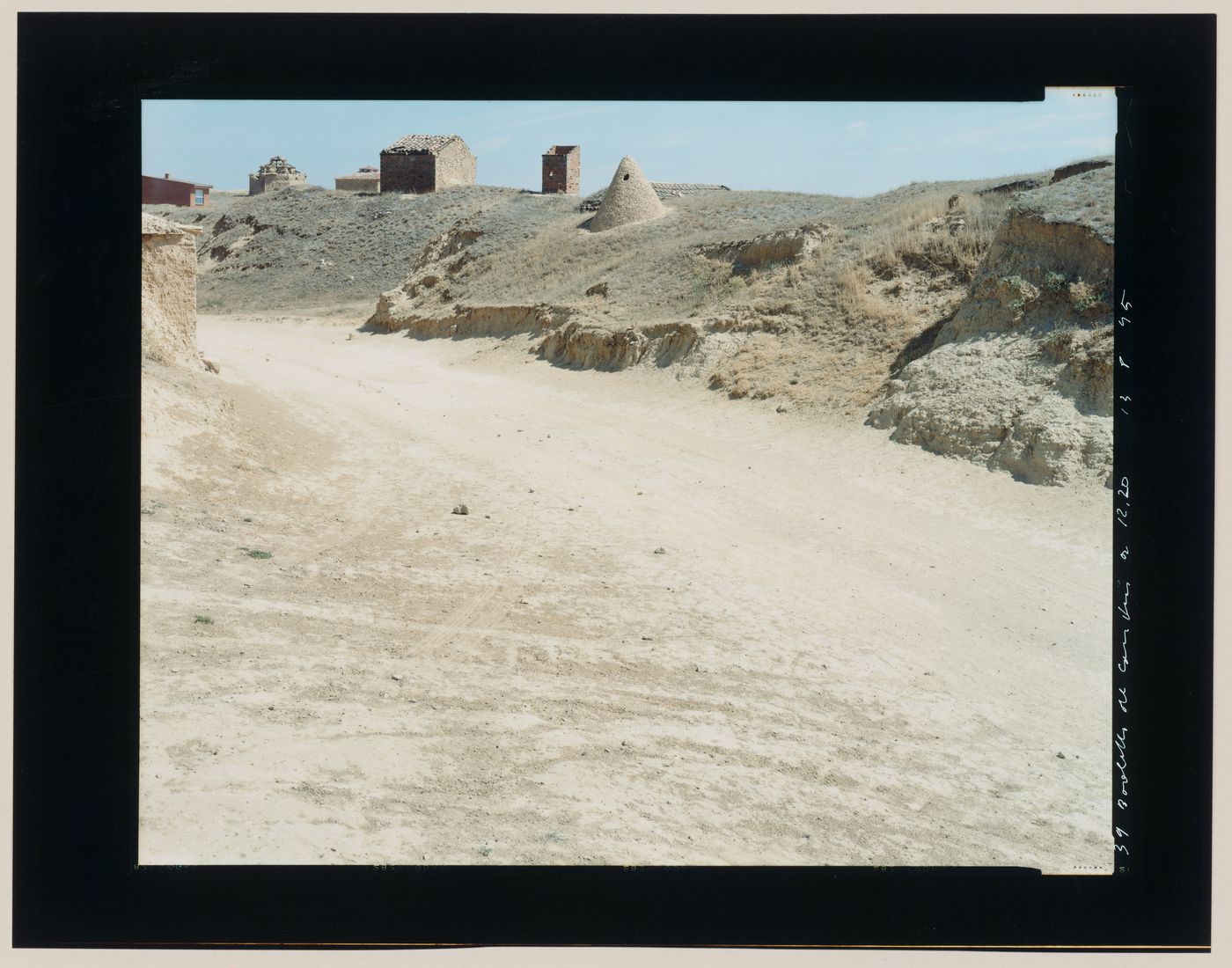 View of a dirt road, pigeon lofts and brick structures and an adobe vent probably connected to an underground wine cellar, Boadilla del Camino, Palencia Province, Spain (from the series "In between cities")