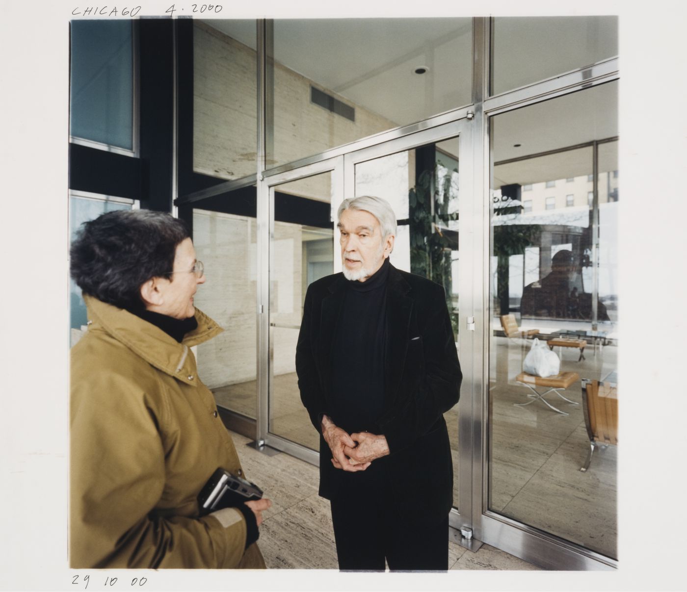 Exterior view of 880 Lake Shore Drive Apartments showing Phyllis Lambert and the architect George Danforth standing in front of the lobby furnished with barcelona chairs, Chicago, Illinois